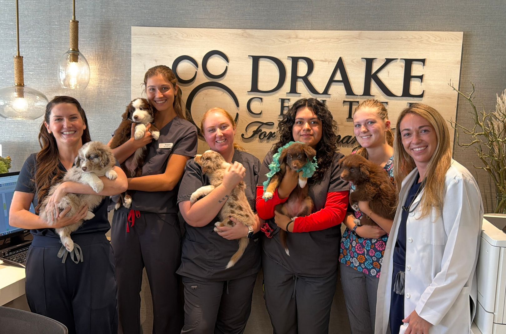 The Drake Center team stands in front of the sign holding puppies.
